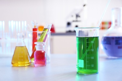 Beaker with color liquid on table against blurred background, space for text.  Chemistry glassware