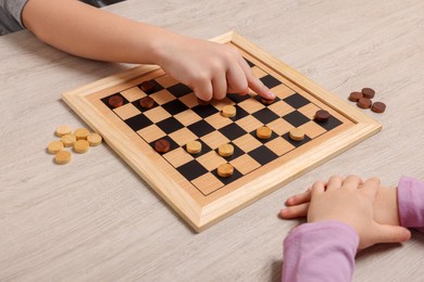 Children playing checkers at light wooden table, closeup