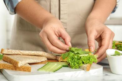 Photo of Woman making tasty sandwich at white marble table, closeup