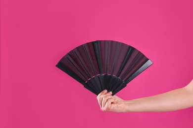 Photo of Woman holding black hand fan on pink background, closeup
