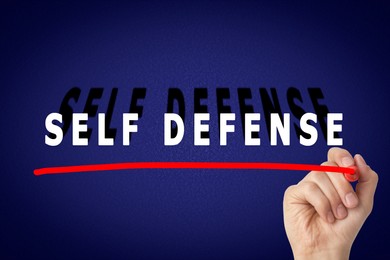 Image of Man underlining words Self Defense with marker glass board against blue background, closeup