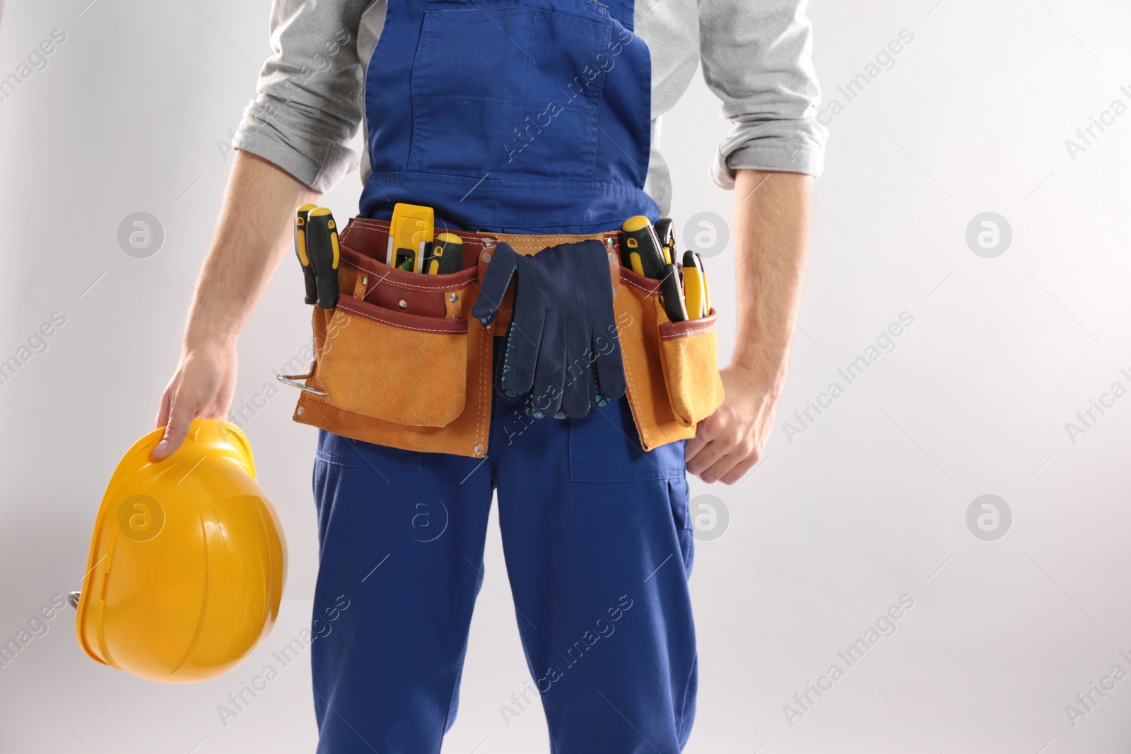 Photo of Construction worker with hard hat and tool belt on light background, closeup. Space for text