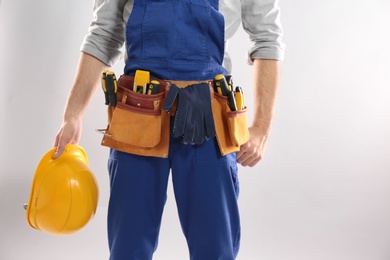 Photo of Construction worker with hard hat and tool belt on light background, closeup. Space for text