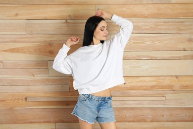 Photo of Portrait of young woman in sweater at wooden wall. Mock up for design