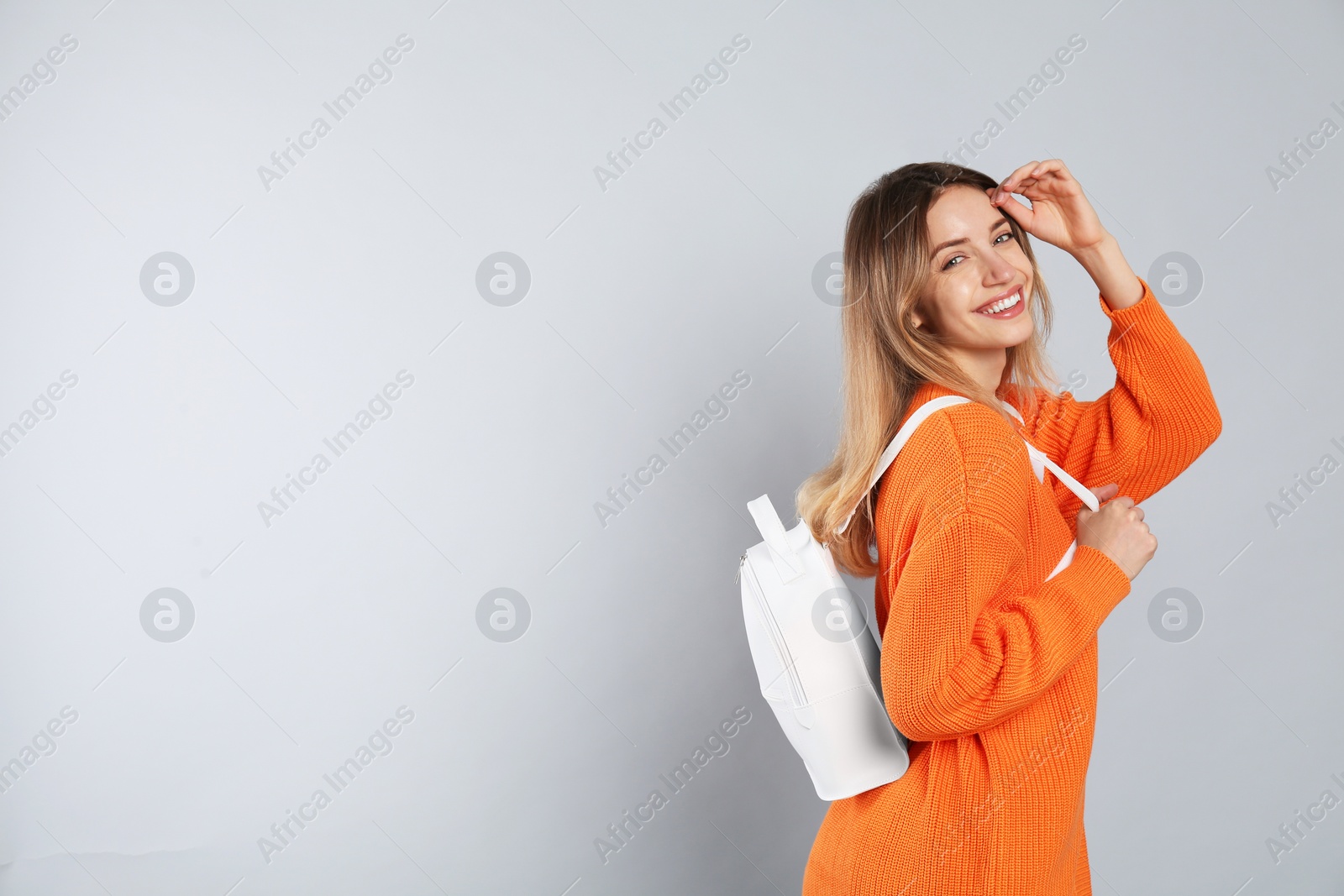 Photo of Happy woman with backpack on light grey background. Space for text