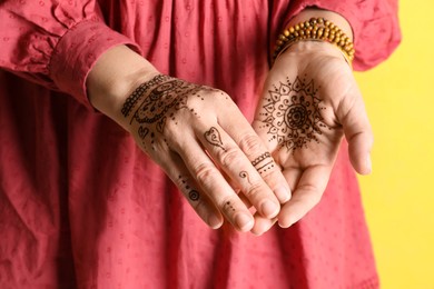 Photo of Woman with beautiful henna tattoos on hands against yellow background, closeup. Traditional mehndi