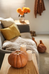 Pumpkin and burning candles on wooden table in room. Cozy interior inspired by autumn colors