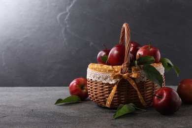 Photo of Ripe red apples and leaves in wicker basket on dark grey table. Space for text