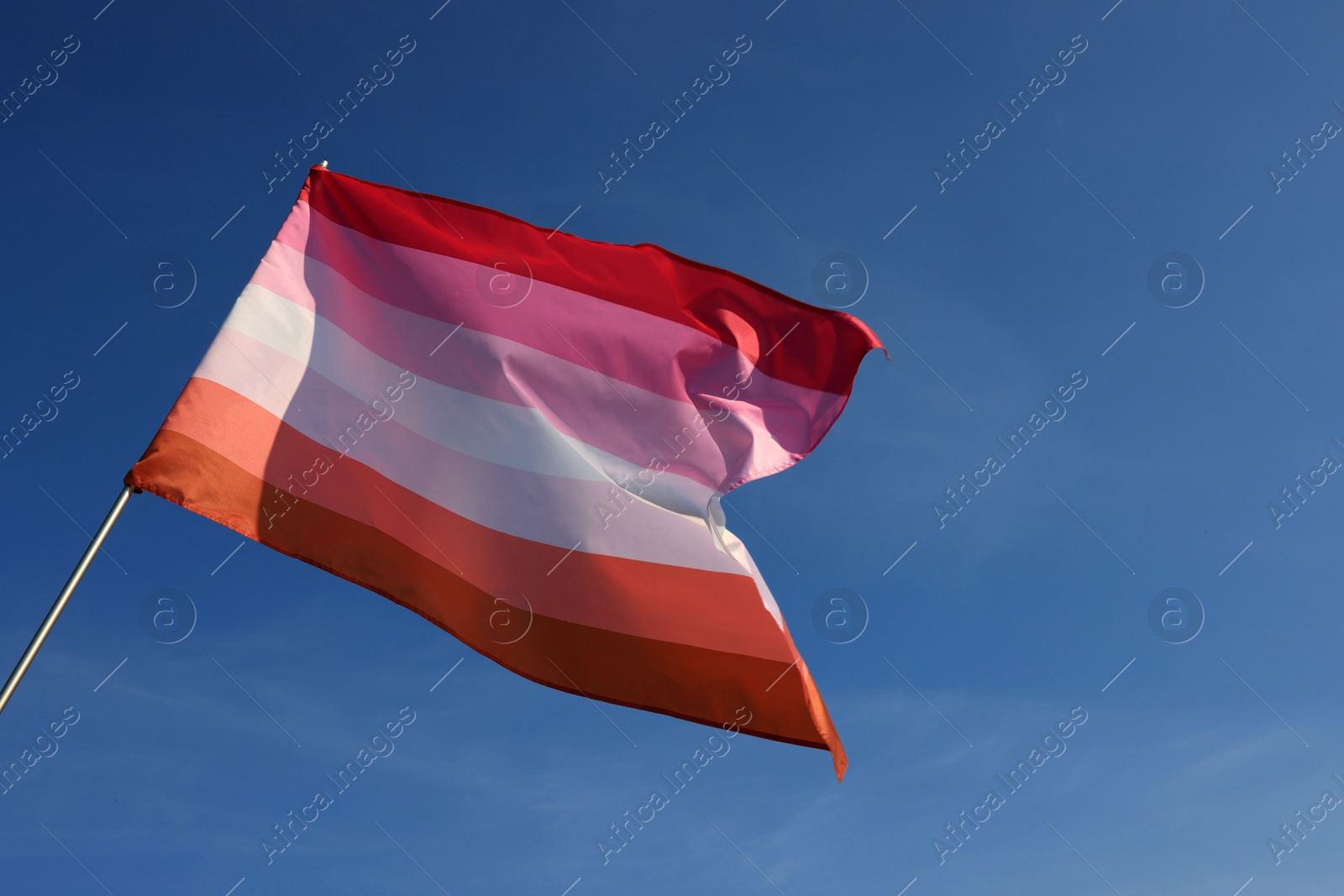 Photo of Bright lesbian flag fluttering against blue sky, low angle view. Space for text