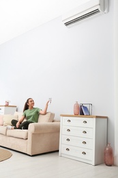 Photo of Happy young woman switching on air conditioner with remote control at home