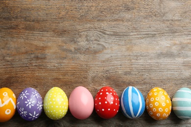 Flat lay composition of painted Easter eggs on wooden table, space for text