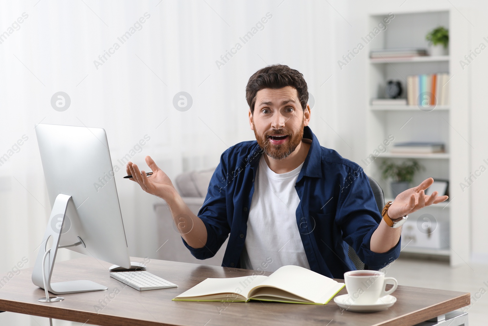 Photo of Home workplace. Emotional man at wooden desk with computer in room