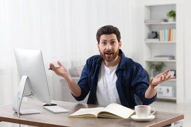 Home workplace. Emotional man at wooden desk with computer in room