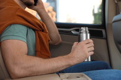 Man with thermos talking on phone in car, closeup