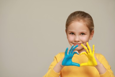 Little girl making heart with her hands painted in Ukrainian flag colors on light grey background, space for text. Love Ukraine concept