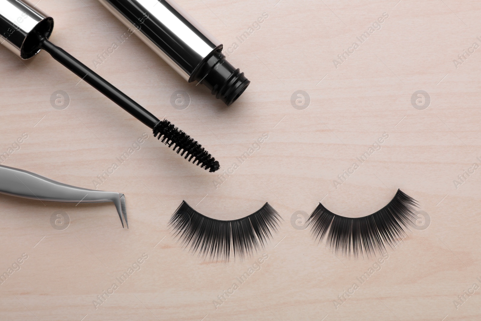Photo of Flat lay composition with false eyelashes, mascara brush and tweezers on wooden table