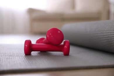 Photo of Pink dumbbells with grey yoga mat on floor in room. Home fitness