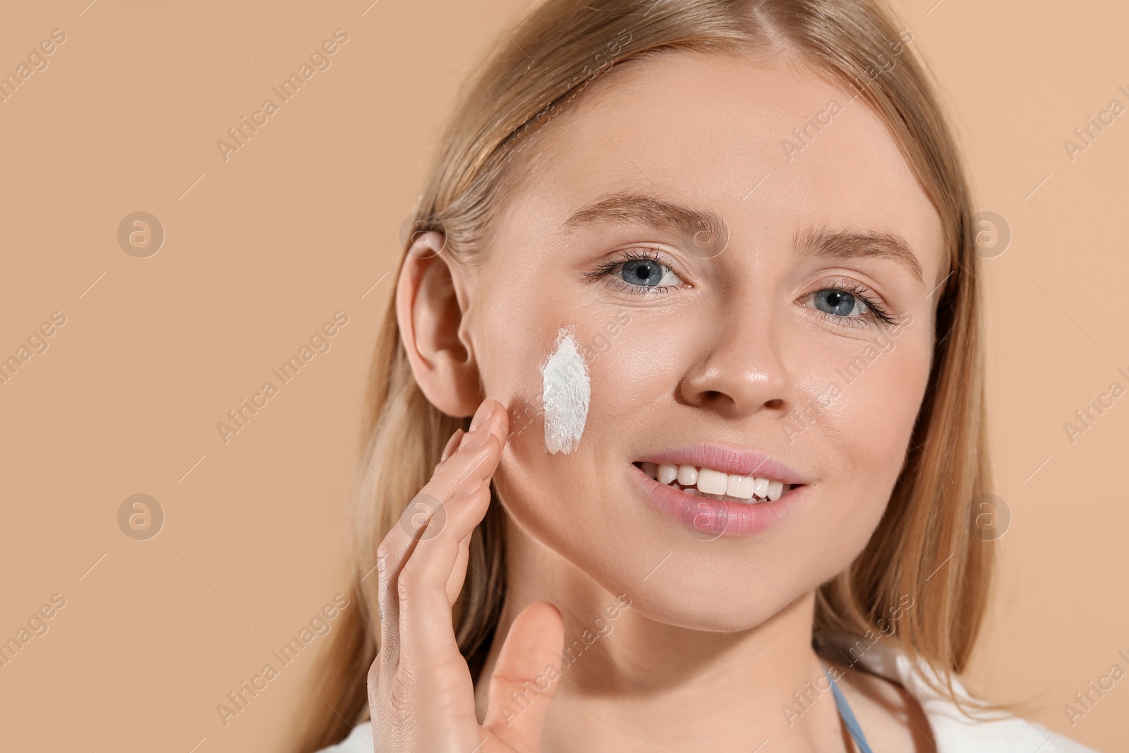 Photo of Beautiful young woman with sun protection cream on her face against beige background, space for text