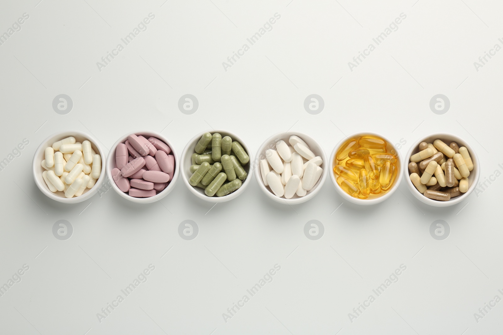 Photo of Different vitamin capsules in bowls on white background, flat lay