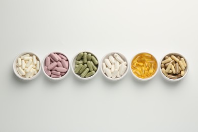 Different vitamin capsules in bowls on white background, flat lay