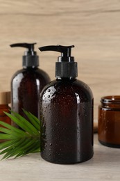 Shampoo bottles, essential oil, hair mask and green leaf on white wooden table