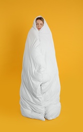 Young woman wrapped in soft blanket on yellow background