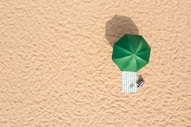 Image of Beach umbrella near towel and other vacationist's stuff on sand, aerial view. Space for text