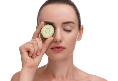 Beautiful woman covering eye with piece of cucumber on white background