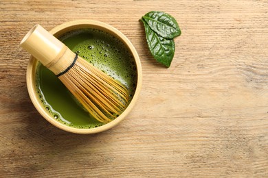 Photo of Cup of fresh matcha tea with bamboo whisk and leaves on wooden table, flat lay. Space for text