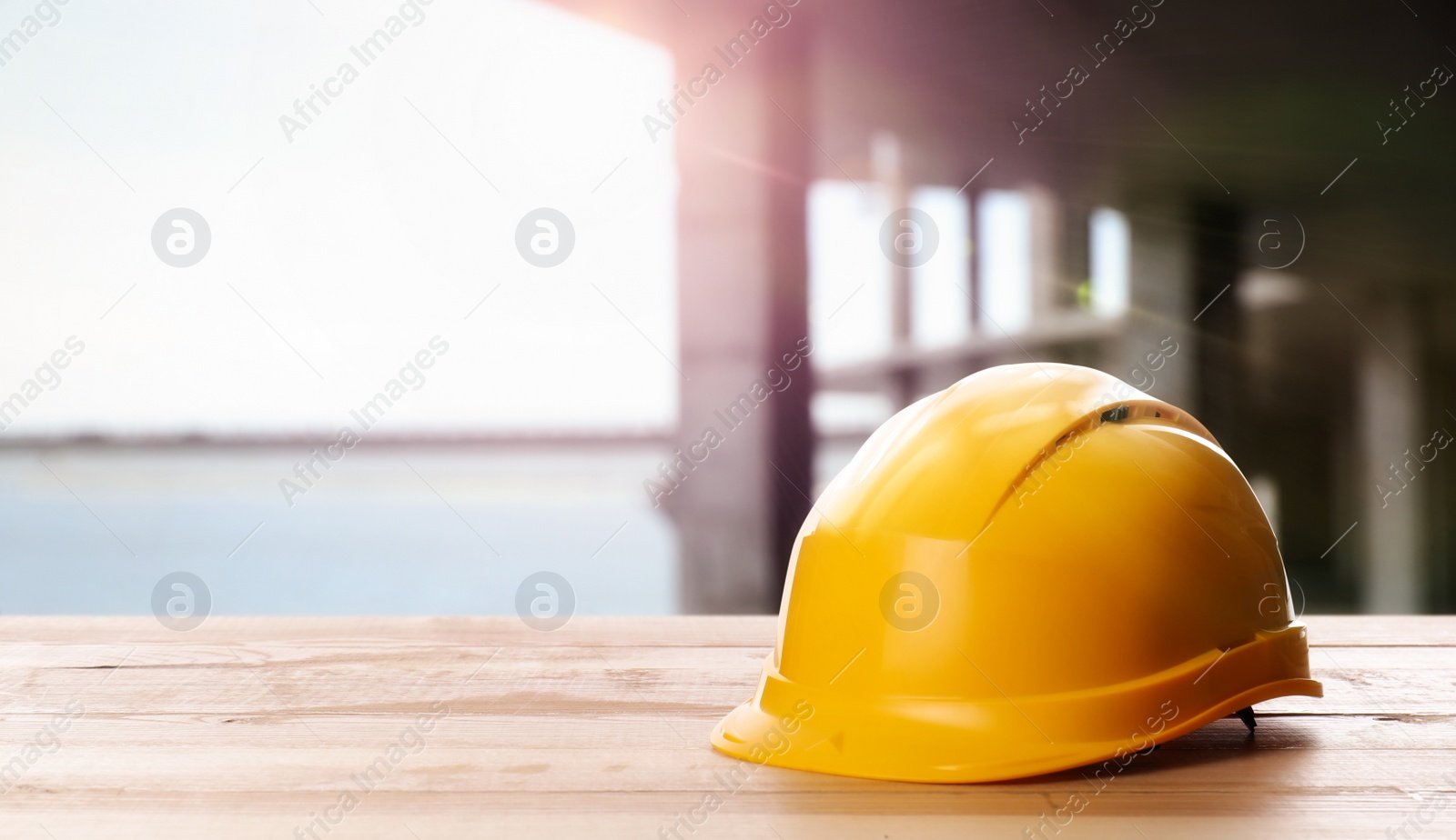 Image of Hard hat on wooden surface at construction site with unfinished building. Space for text 