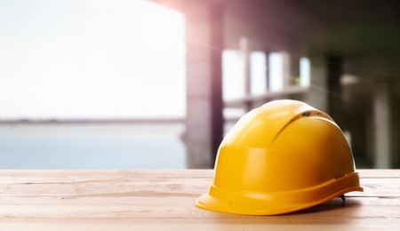 Image of Hard hat on wooden surface at construction site with unfinished building. Space for text 