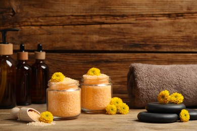 Jars with orange sea salt, spa stones, towel and beautiful flowers on wooden table