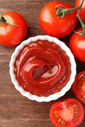 Bowl of tasty ketchup and tomatoes on wooden table, flat lay