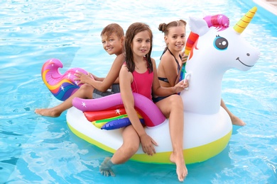 Photo of Happy children on inflatable unicorn in swimming pool