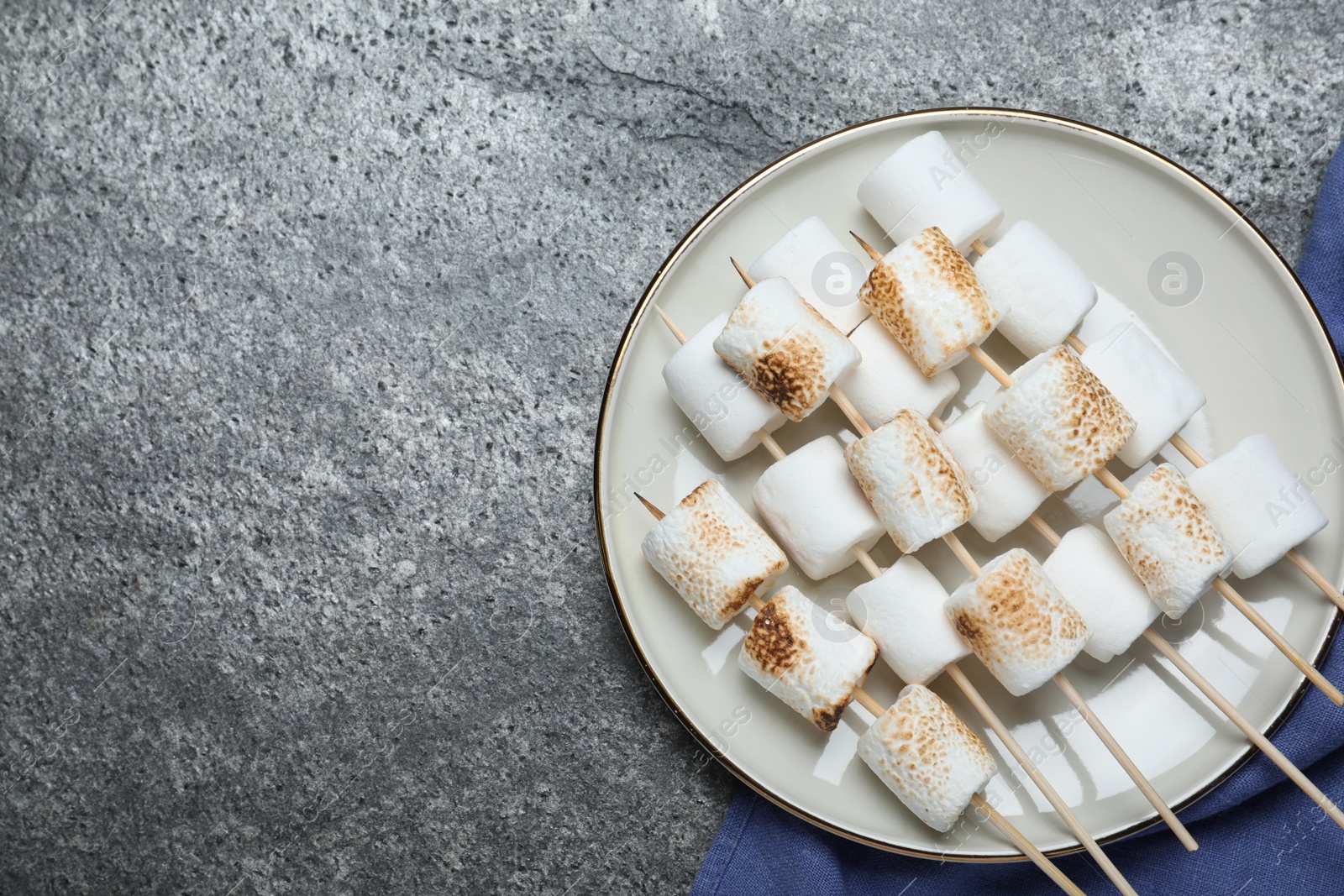 Photo of Sticks with roasted marshmallows on grey table, flat lay. Space for text