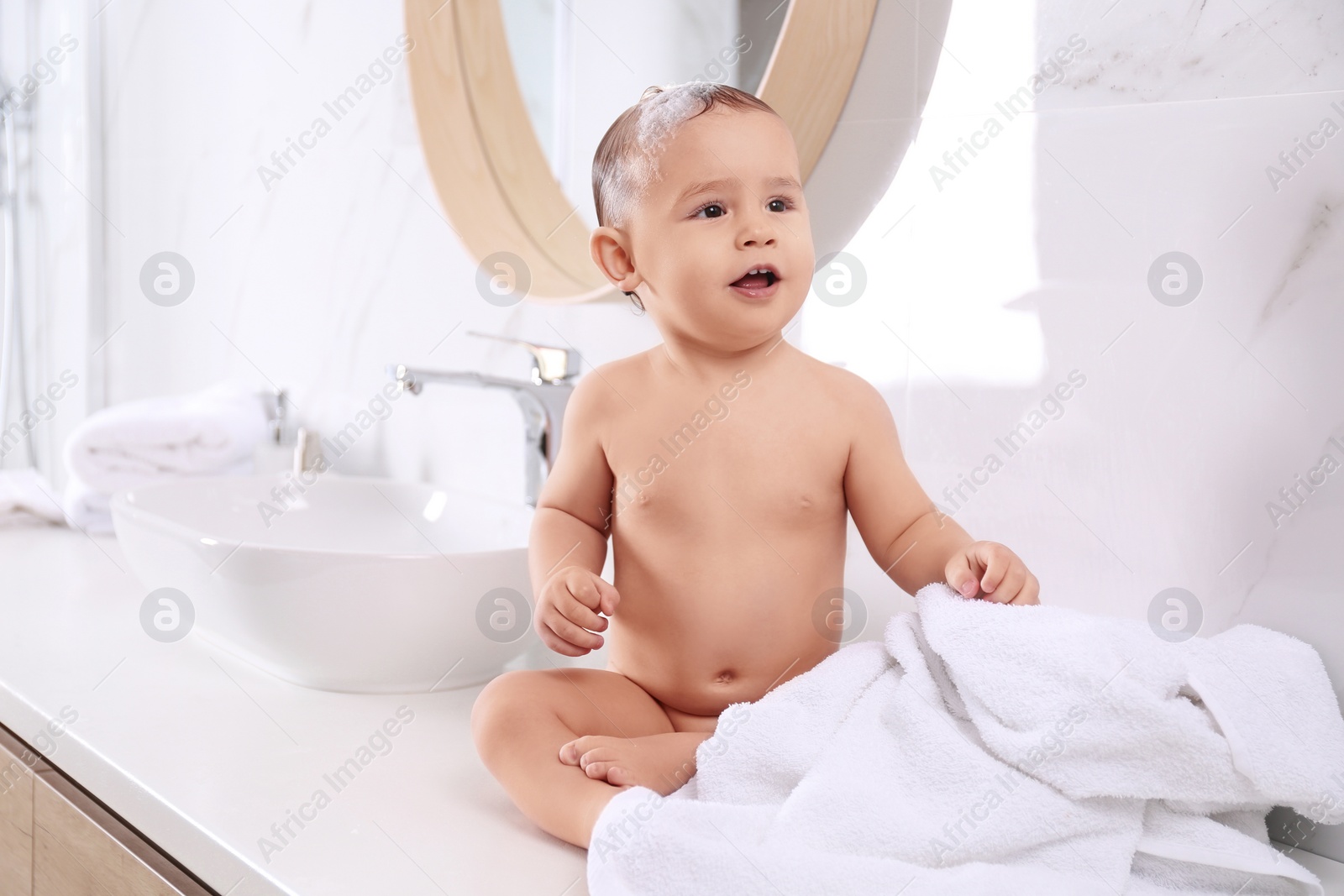 Photo of Cute little baby sitting on countertop in bathroom