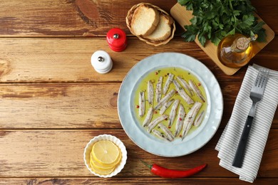 Tasty pickled anchovies with spices and products on wooden table, flat lay. Space for text