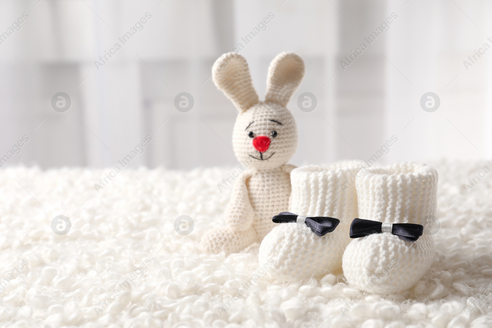 Photo of Handmade baby booties and stuffed rabbit on plaid against blurred background. Space for text