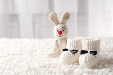 Handmade baby booties and stuffed rabbit on plaid against blurred background. Space for text