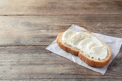 Photo of Slice of bread with tasty cream cheese on wooden table, space for text