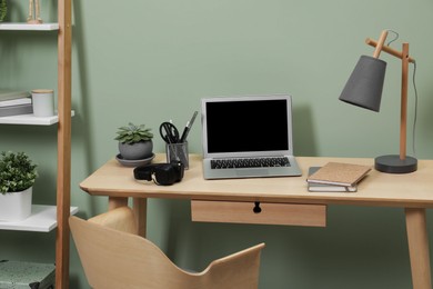 Workplace with laptop, stationery on desk and chair in home office