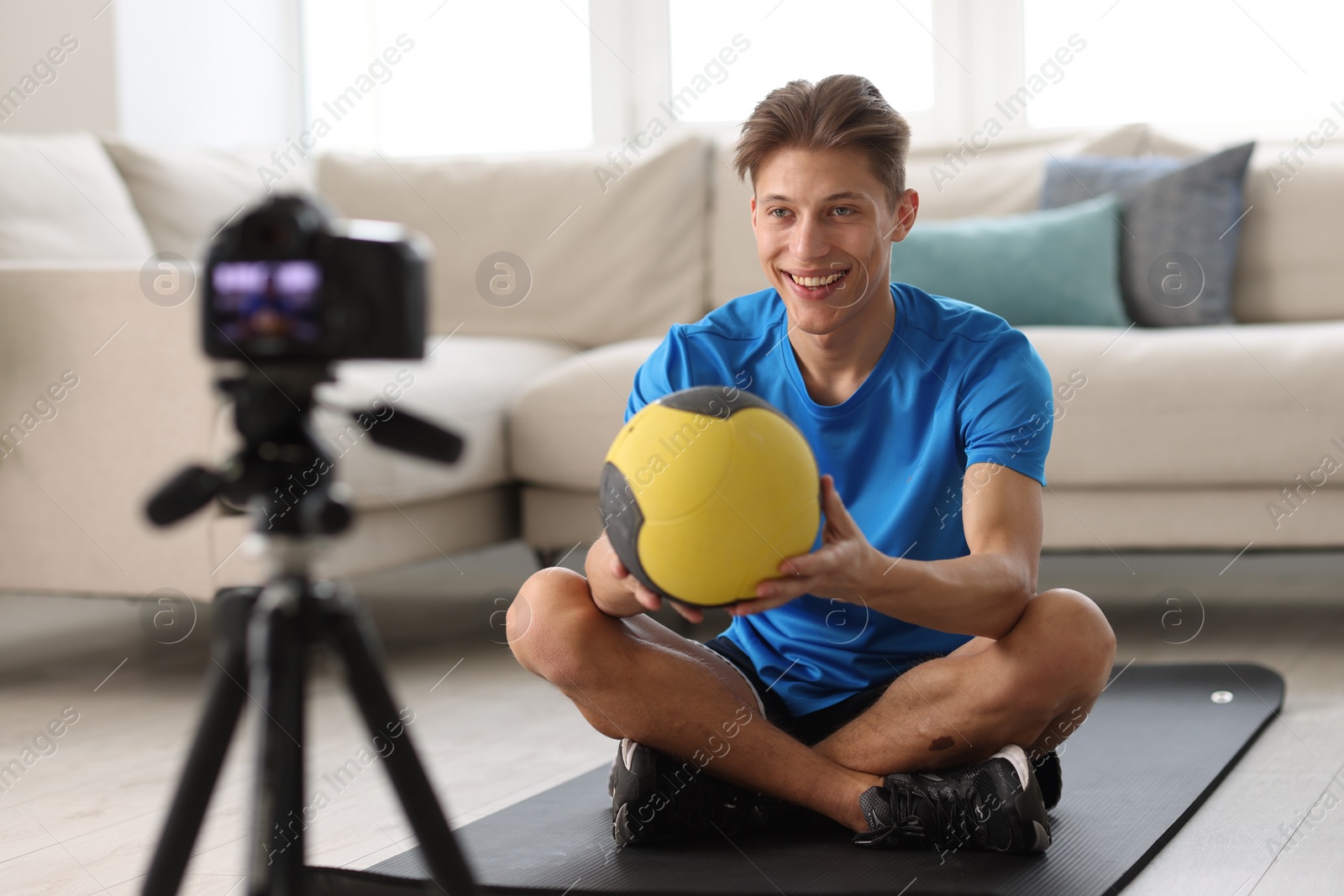 Photo of Smiling sports blogger holding medicine ball while recording fitness lesson with camera at home