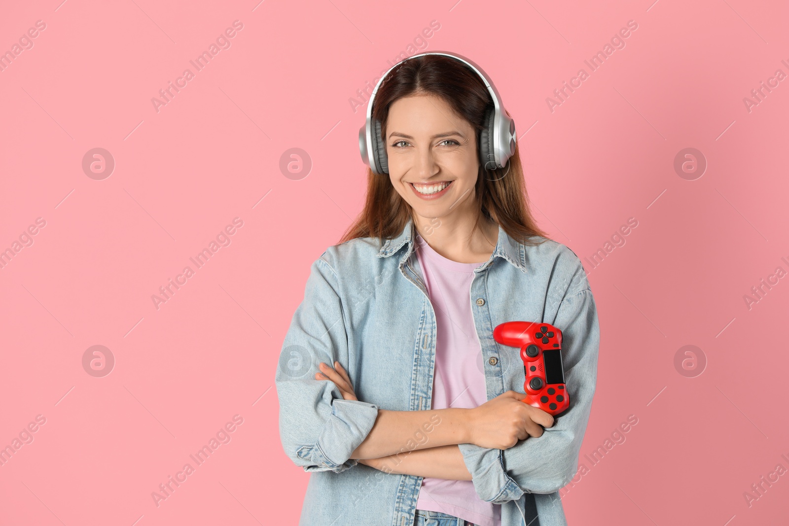 Photo of Happy woman in headphones with game controller on pink background. Space for text