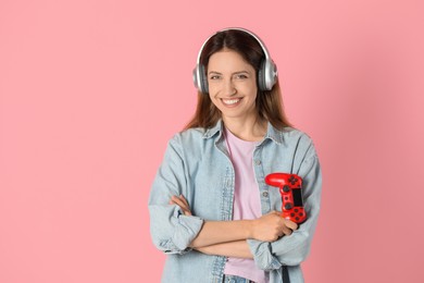 Photo of Happy woman in headphones with game controller on pink background. Space for text