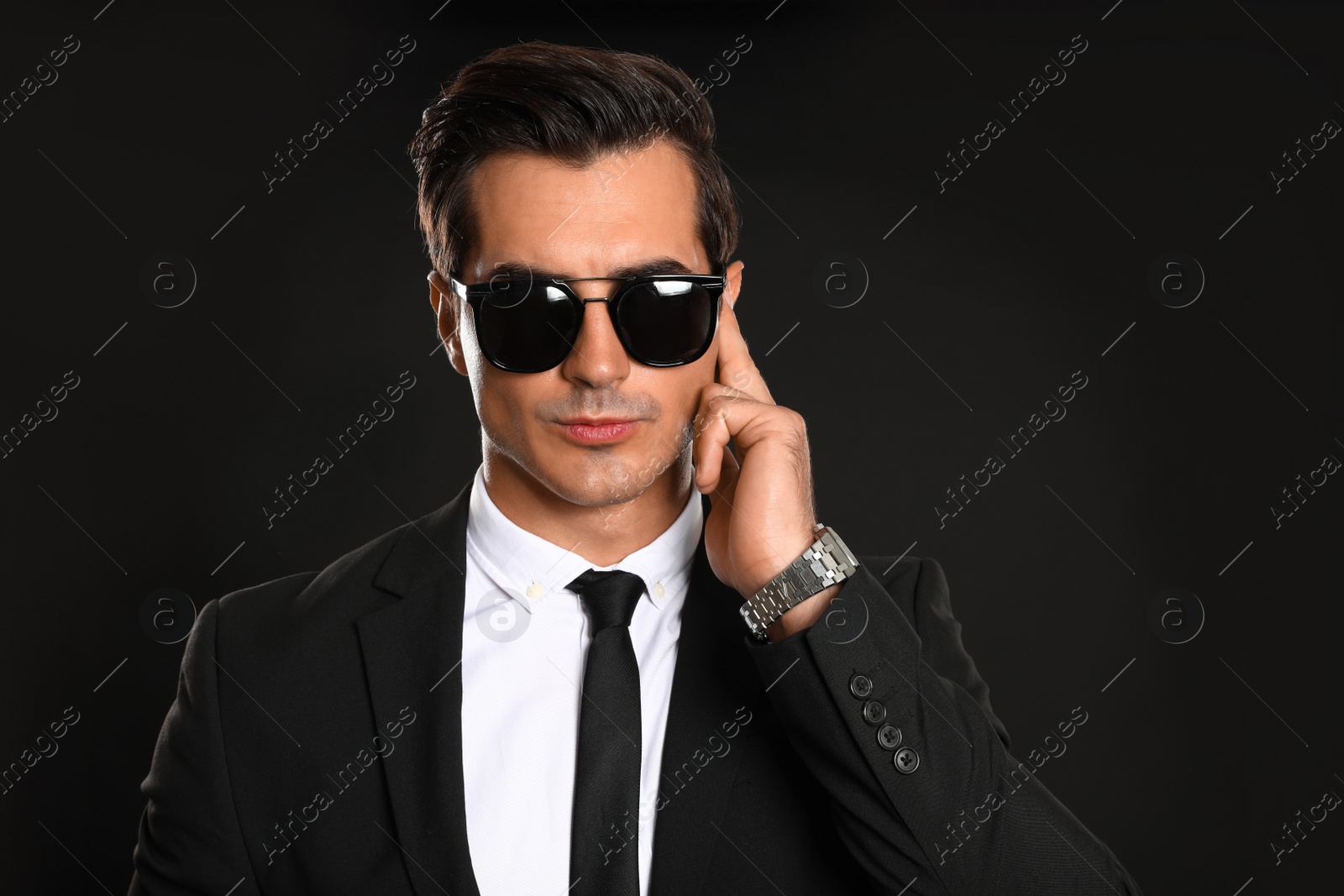 Photo of Male security guard in uniform using radio earpiece on dark background