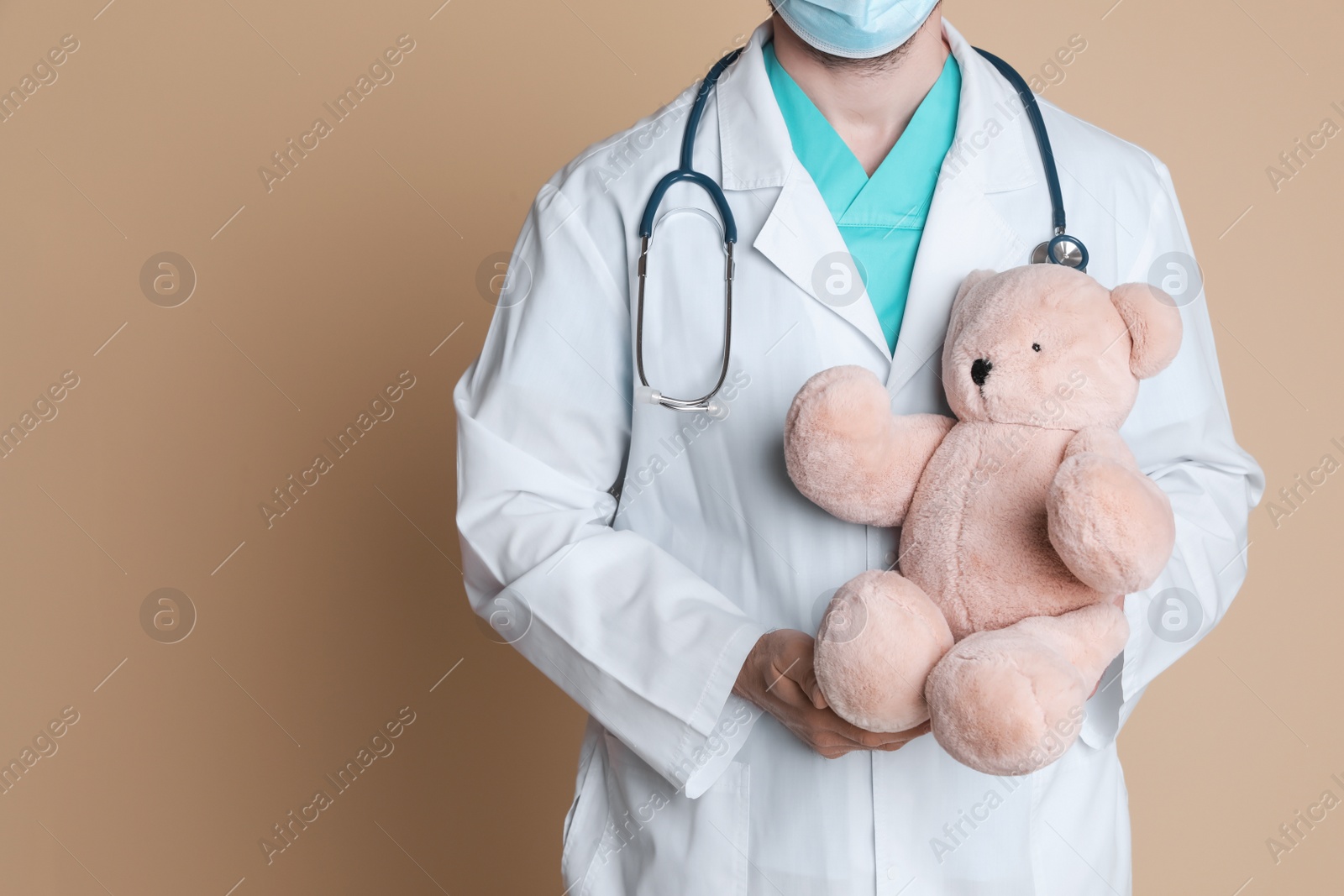 Photo of Pediatrician with teddy bear and stethoscope on beige background, closeup. Space for text