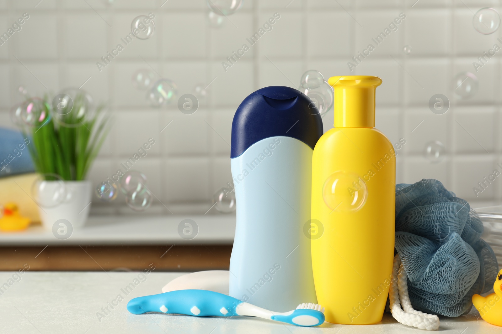 Photo of Baby cosmetic products, bath duck, toothbrush and sponge on white table against soap bubbles. Space for text