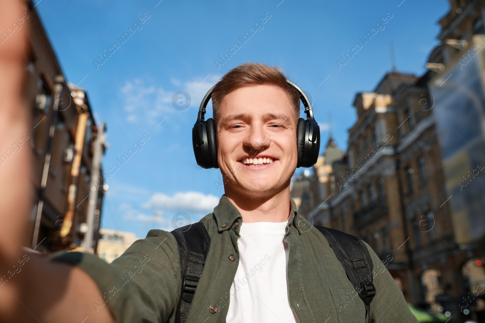 Photo of Smiling man in headphones taking selfie on city street