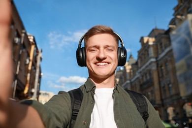 Photo of Smiling man in headphones taking selfie on city street
