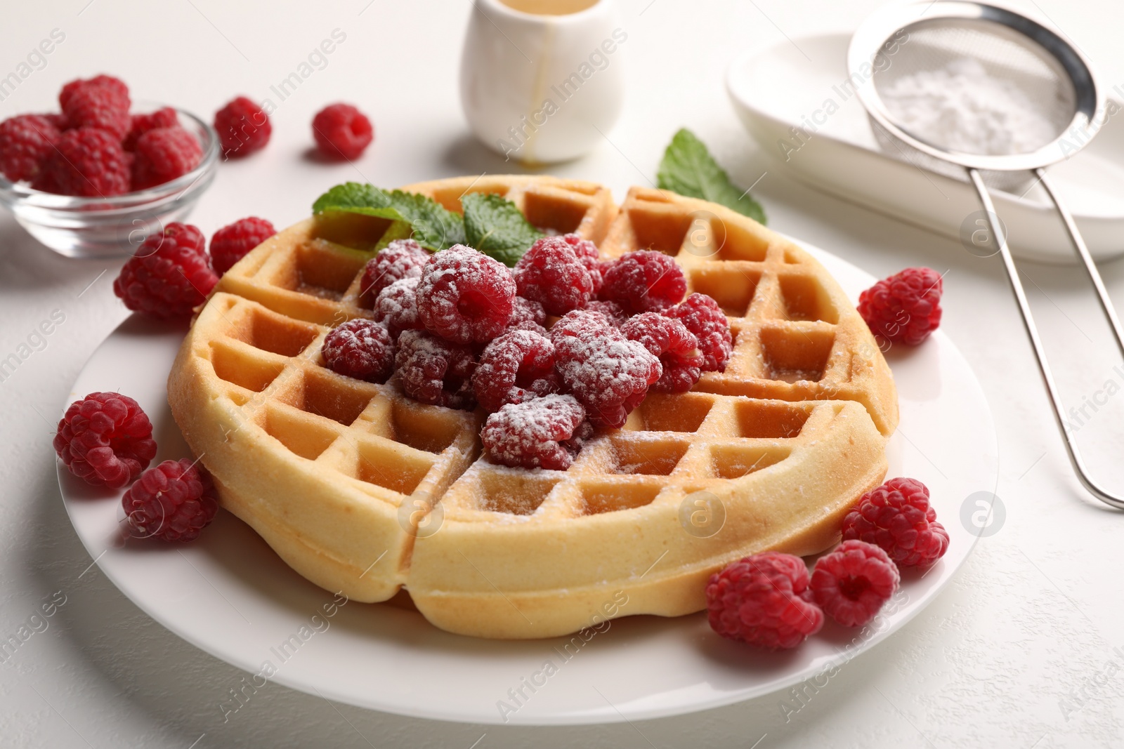 Photo of Tasty Belgian waffle with fresh raspberries, powdered sugar and mint on white table, closeup